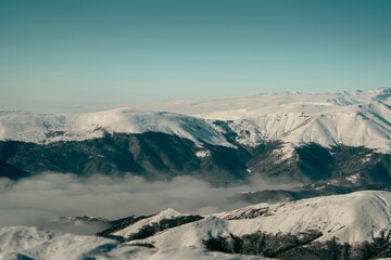 Fototapeta premium Snow-covered mountains under a clear blue sky with clouds in the valley.