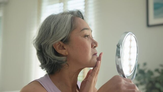 Asia adult people middle age old woman look at mirror dry skin face hand touch neck cheek stress sad at home elder health care aging beauty issue. Asian female aged eye botox filler plastic surgery.
