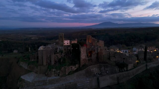 Aerial view of Celleno, a picturesque village in the Province of Viterbo, Italy, illuminated at dusk, showcasing its ancient ruins and surrounding landscape