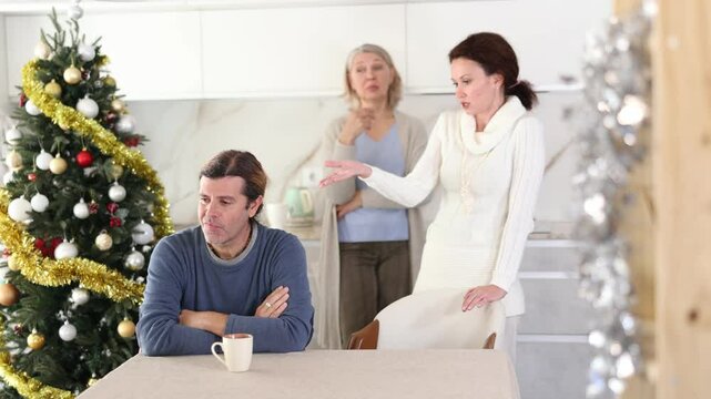 On Christmas Eve elderly mother and woman scold swear at man. Man is upset because of family conflict, dejectedly listens to his wife and mother scolding him. Complex intergenerational relationships