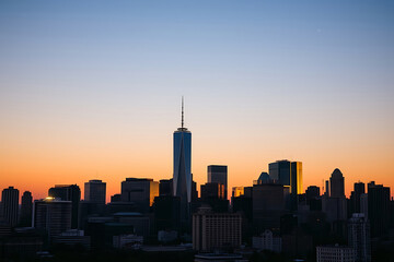 Fototapeta premium City skyline at dusk stock-image with a golden sunset glow illuminating towering skyscrapers, casting vibrant reflections on glass windows, under 