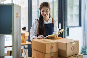 Young woman engaged in online business working with using notebook, preparing package for shipping...