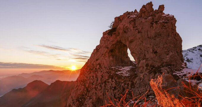 Stunning timelapse video of the Porta di Prada rock formation in Alpe Cainallo, with the sun rising over the rugged mountainous landscape and casting a warm glow on the snow-covered terrain