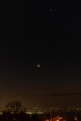 Earthshine illuminates the night side of the crescent moon over a cityscape