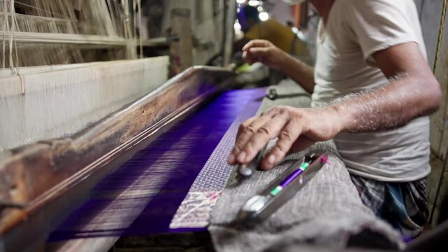 Old experienced Indian artisan hand weaving a Banarasi silk saree on a traditional wooden handloom. Adding thread to the weft shuttle