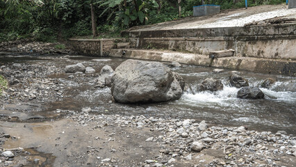 The river flows gently between sturdy rocks and the natural soil, creating a tranquil harmony