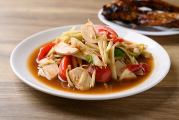 Thai food (Som Tum), Spicy papaya salad with pork sausage eating with grilled chicken wing. Local Thai food