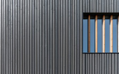 Dark gray wood paneling forms a textured background, featuring a small square window with vertical wooden bars. The image showcases a minimalist architectural detail