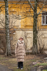 Mature adult attractive woman with blond hair in a demi-season coat against the background of the facade of an ancient building.