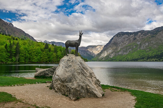 Majestic Zlatorog statue standing on a rock by the serene Lake Bohinj, surrounded by the breathtaking Julian Alps in Slovenia