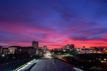 Cherkasy skyline under a colorful sunset with pink, purple, and blue hues illuminating buildings and a road