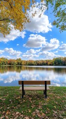 Obraz premium Bench Overlooking Calm Lake Reflecting Autumn Trees and Cloudy Sky