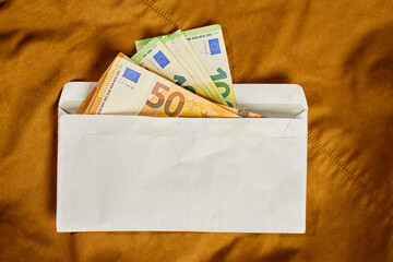 Euro banknotes inside white envelope, top view. Close up of cash money on brown background. Concept...