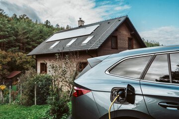 Electric car charging in front of house with solar panels on roof.