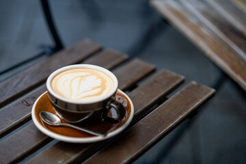 Cup of cappuccino with latte art on wooden table, cozy cafe setting.