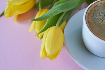 Yellow tulips and a cup of coffee on a pink background.