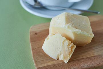 Parmesan cheese on a wooden plank on a green background.