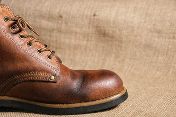 Close-up of a worn brown leather boot with visible creases, patina, and sturdy stitching. The rustic background enhances the rugged, vintage aesthetic.