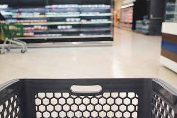 Empty shopping basket standing in the supermarket aisle with refrigerated display case full of groceries in the background, ready for shopping