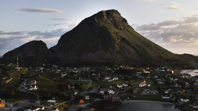 Aerial drone shot panning to the left showing the Island of Lovund with the summit of Lovundfjellet towering over the village. Lovund, Norway