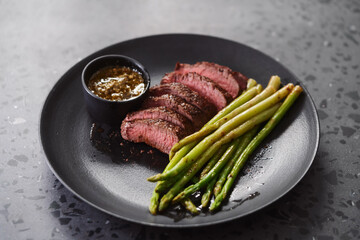 New york steak with asparagus on black plate with pesto sauce