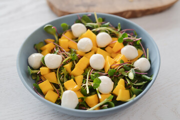 Salad with mango, mozzarella and mixed microgreens in blue bowl on white oak table