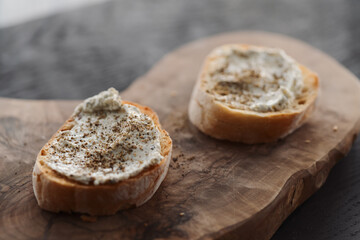 Ciabatta slices with cream cheese and herbs on olive wood board