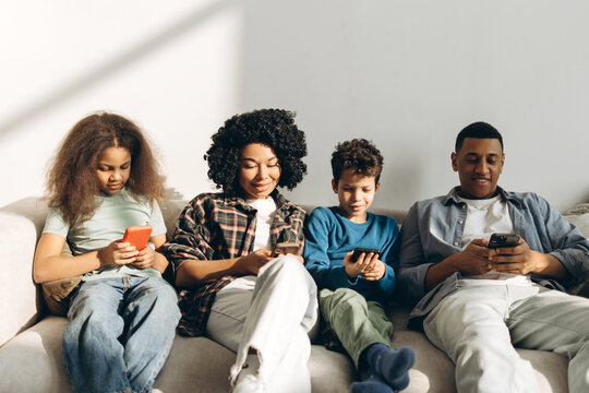 Smiling, happy African American family using smartphones sitting on couch at home