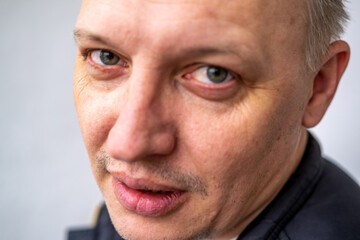Portrait of a cheerful middle-aged man wearing a gray hoodie, standing against a textured stone wall in natural light.