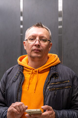 Portrait of a cheerful middle-aged man wearing a gray hoodie, standing against a textured stone...