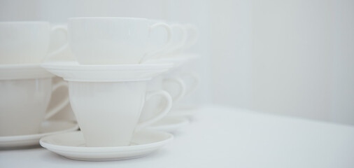 Lots of empty tea or coffee cups on a white table against a white wall, space for text.  Organization of events, catering, catering, beautiful white and gray background