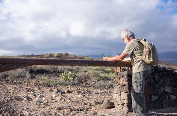 Senior white haired man enjoying outdoor adventure stops checking a map. Active mature man in mountain and countryside excursion