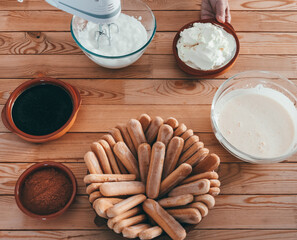 Top view of a woman using electric mixer to make tiramisu, cheesecake with coffee, mascarpone and biscuits. Rustic wooden table