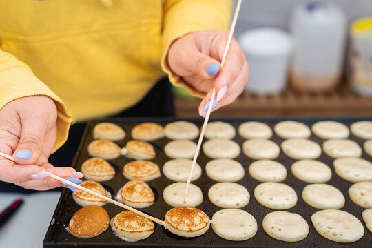 Typical Dutch poffertjes - tiny pancakes-being baked on a heavy cast iron pan being prepared during street food festival, an outdoor event. Making mini pancakes on the pancake machine. 