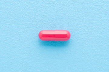 Red capsule for improve of iron level in blood on light blue table background. Pastel color. Closeup. Top down view.