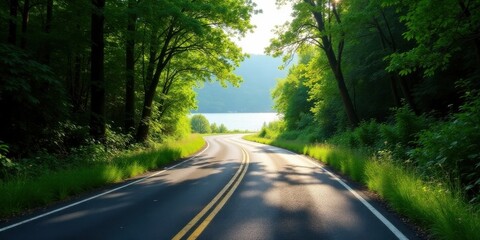 Scenic winding road through lush green forest with a tranquil lake view at sunrise