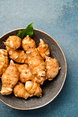 Organic raw Jerusalem artichoke root in a ceramic bowl. On a gray stone background. Close-up. Free space for text.