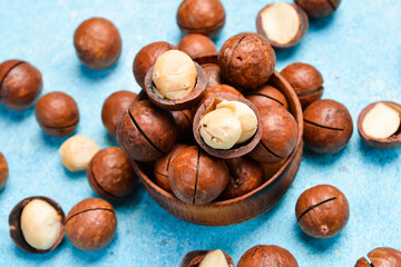 Macadamia nuts in a bowl on a blue stone background. Close-up, side view.