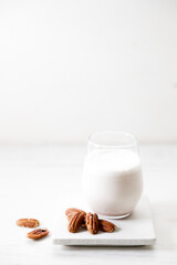 Pecan milk in a glass with raw pecan nuts on wooden table.