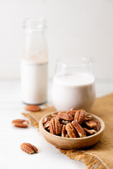 Pecan milk in a glass with raw pecan nuts on wooden table.