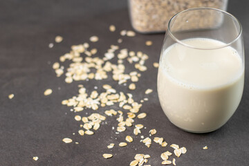 A glass of oat milk and oatmeal in a box on grey kitchen table. Vegan and non-dairy alternative milk
