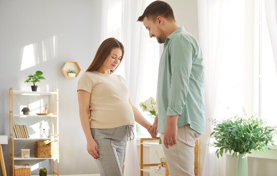 Loving couple young future parents expecting first baby close standing at home, caring husband and pregnant wife, expressing love, caress, parenthood, new life, planning, dreaming, prenatal care 
