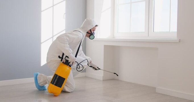Man in protective suit and mask disinfecting room in apartment, fighting against insects, spraying special liquid, working on safe living environment at home. Male pest control worker