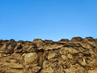 Dilapidated fortress stone wall of ancient fortress against background of blue clear sky. Weathered limestone. Copy space for text.