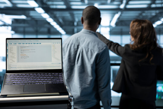 Focus on lines of code on laptop screen used by data center engineers in blurry background to execute security patches. Close up of script on notebook ran by server hub employees scanning equipment