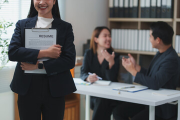 Smiling businesswoman holding resume while recruiters are discussing in the background