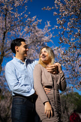 Fototapeta premium Young latin couple embracing under blooming almond trees in springtime
