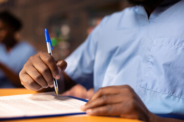 Black med student in scrubs does research and takes notes for his thesis, working hard at the...