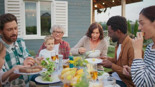 People having nice lunch together outside of house on green lawn. Enjoying warm weather. Placing food on dishes. Enjoying meal in cozy family gathering outside. Sunny warm weather.