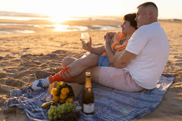 Couple enjoying romantic sunset picnic on beach with wine and flowers